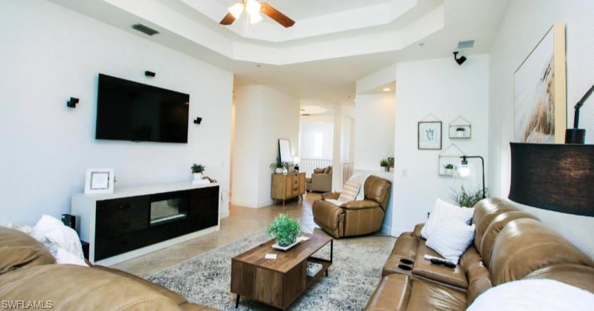 Living area featuring a tray ceiling, a ceiling fan, and tile patterned floors