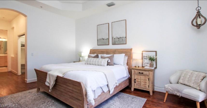 Bedroom with arched walkways, dark wood-style flooring, and connected bathroom