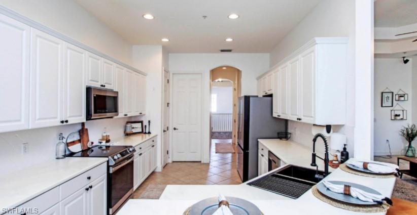 Kitchen featuring arched walkways, stainless steel appliances, light countertops, white cabinets, and recessed lighting
