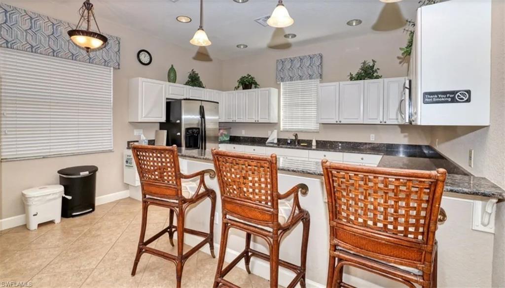 Kitchen with a breakfast bar area, a peninsula, white cabinets, stainless steel appliances, and dark stone countertops