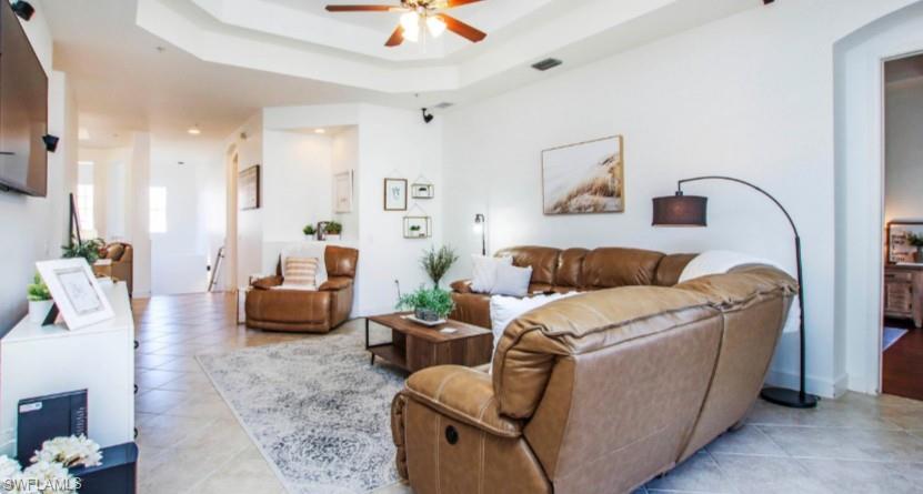 Living area with a raised ceiling, ceiling fan, and light tile patterned floors