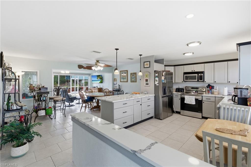 Kitchen featuring stainless steel appliances, decorative light fixtures, light tile patterned flooring, light stone counters, and ceiling fan