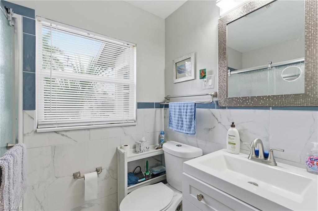 Bathroom featuring a shower stall, vanity, tile walls, and wainscoting