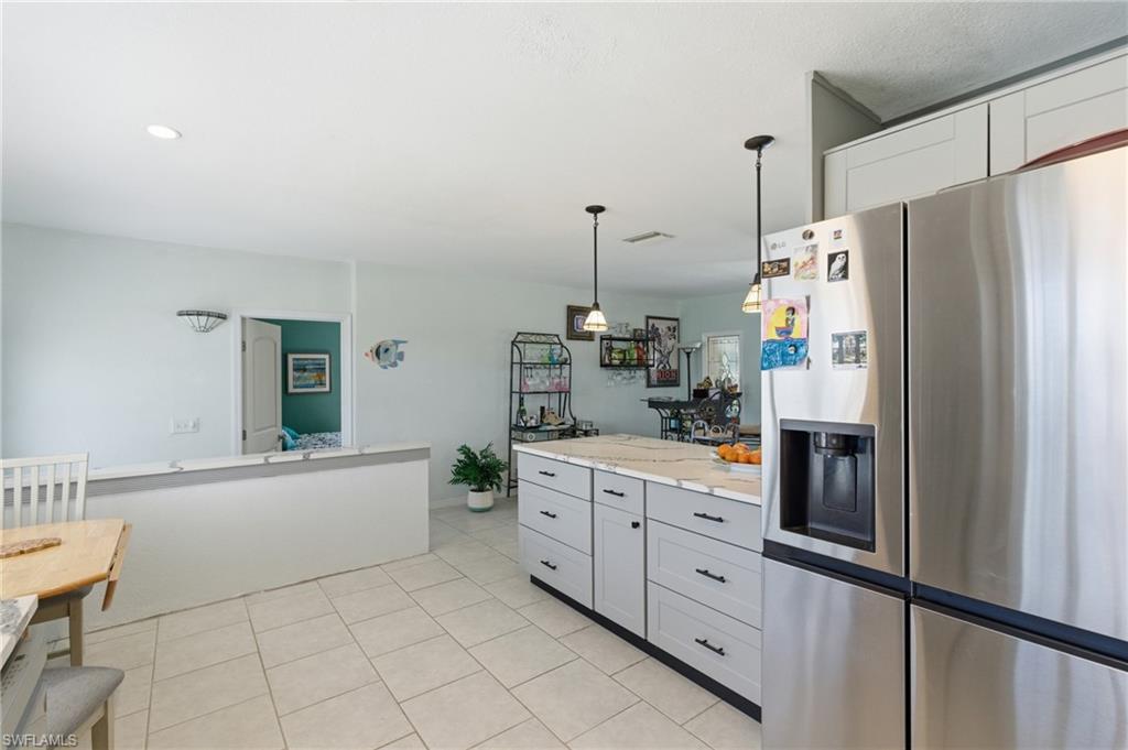 Kitchen featuring stainless steel fridge with ice dispenser, decorative light fixtures, light tile patterned floors, light stone countertops, and white cabinetry