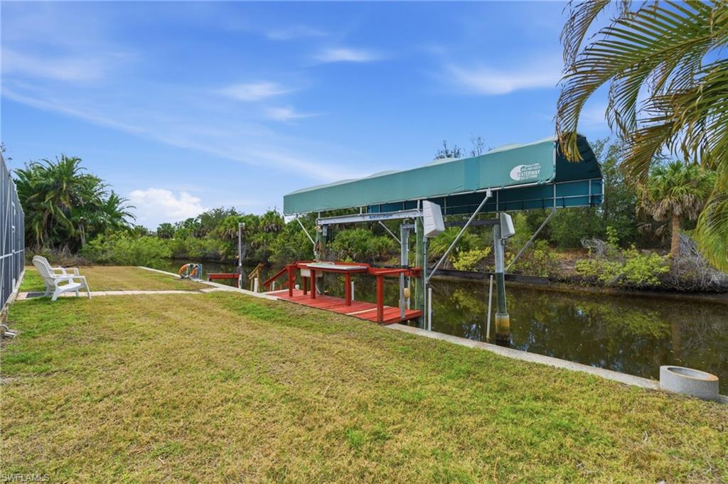 View of grassy yard featuring a water view, boat lift, and a boat dock