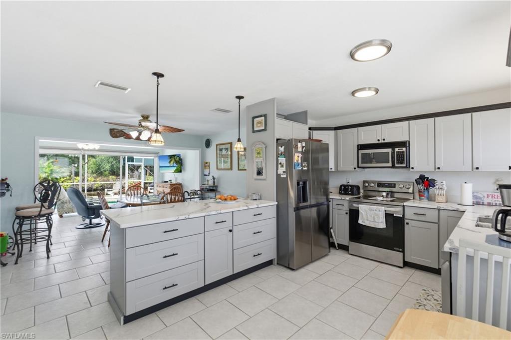 Kitchen with stainless steel appliances, a peninsula, ceiling fan, gray cabinets, and light stone countertops