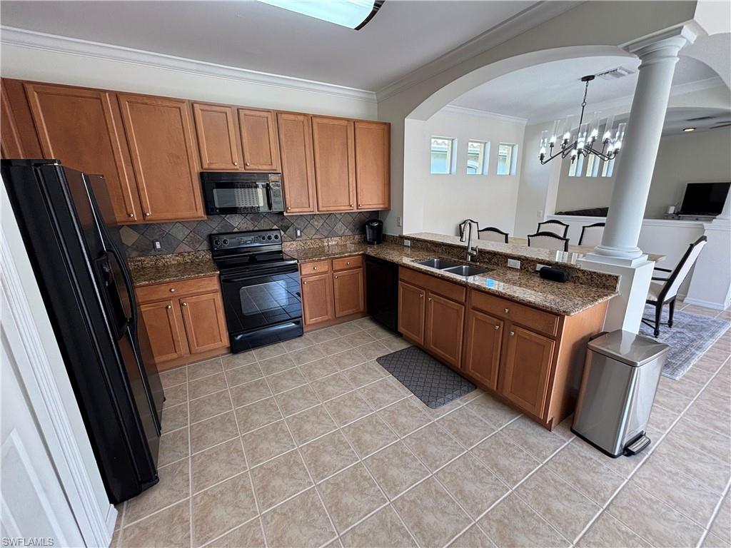 Kitchen with wood finish cabinetry, black appliances, dark stone countertops, light tile patterned flooring, and crown molding