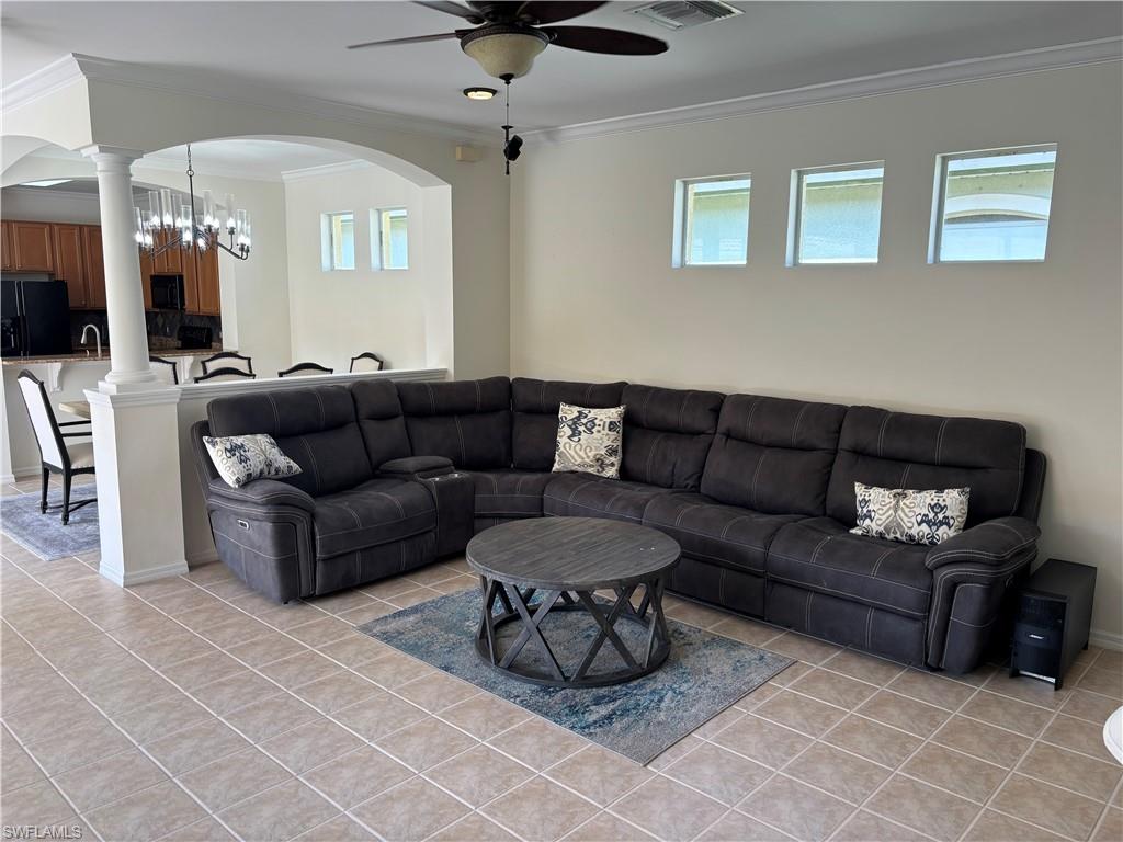 Living area with crown molding, ceiling fan, light tile patterned floors, a chandelier, and arched walkways