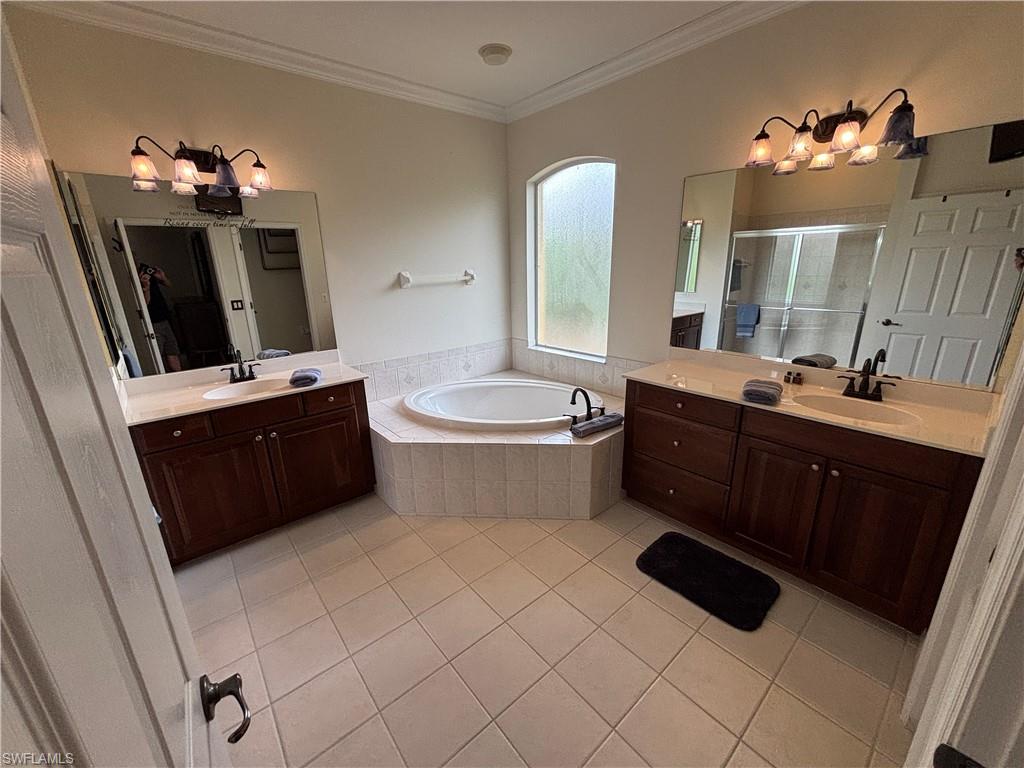 Bathroom featuring suspended lighting, two vanities, crown molding, light tile patterned flooring, and a shower stall