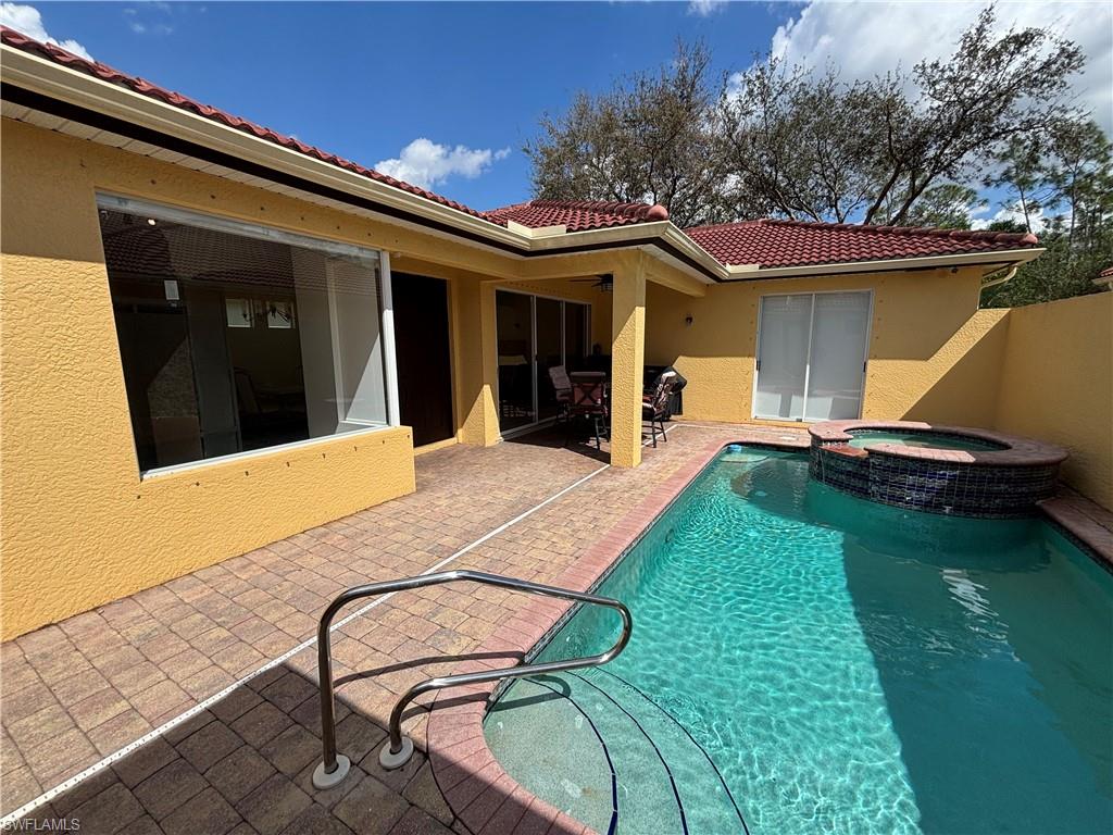 Back of house featuring a patio, stucco siding, and a pool with connected hot tub