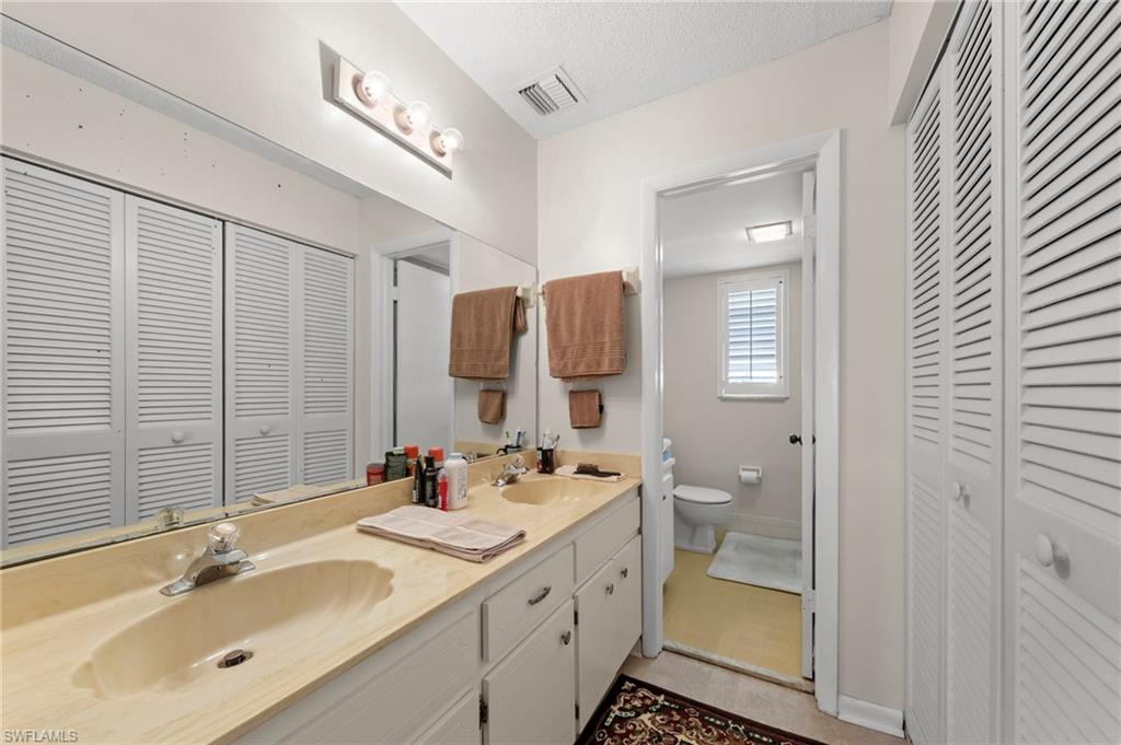 Bathroom with a closet, double vanity, and a textured ceiling