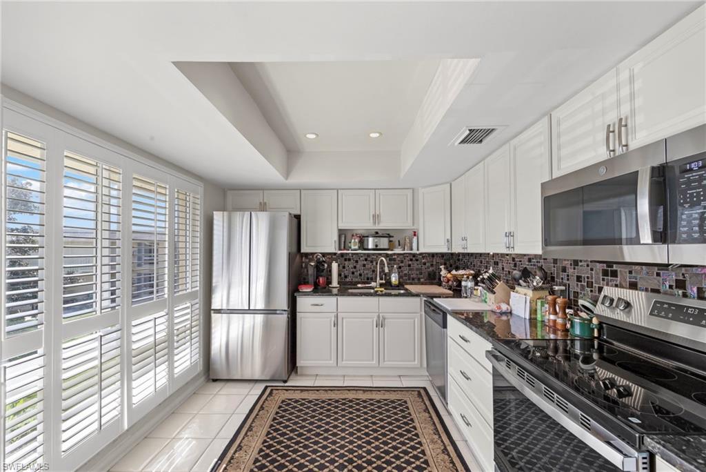 Kitchen with stainless steel appliances, white cabinetry, recessed lighting, a tray ceiling, and light tile patterned floors