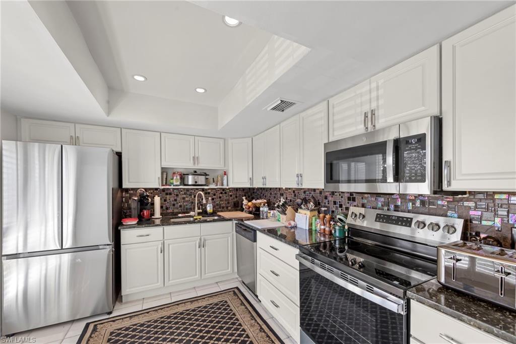 Kitchen featuring stainless steel appliances, white cabinetry, recessed lighting, dark stone countertops, and a tray ceiling