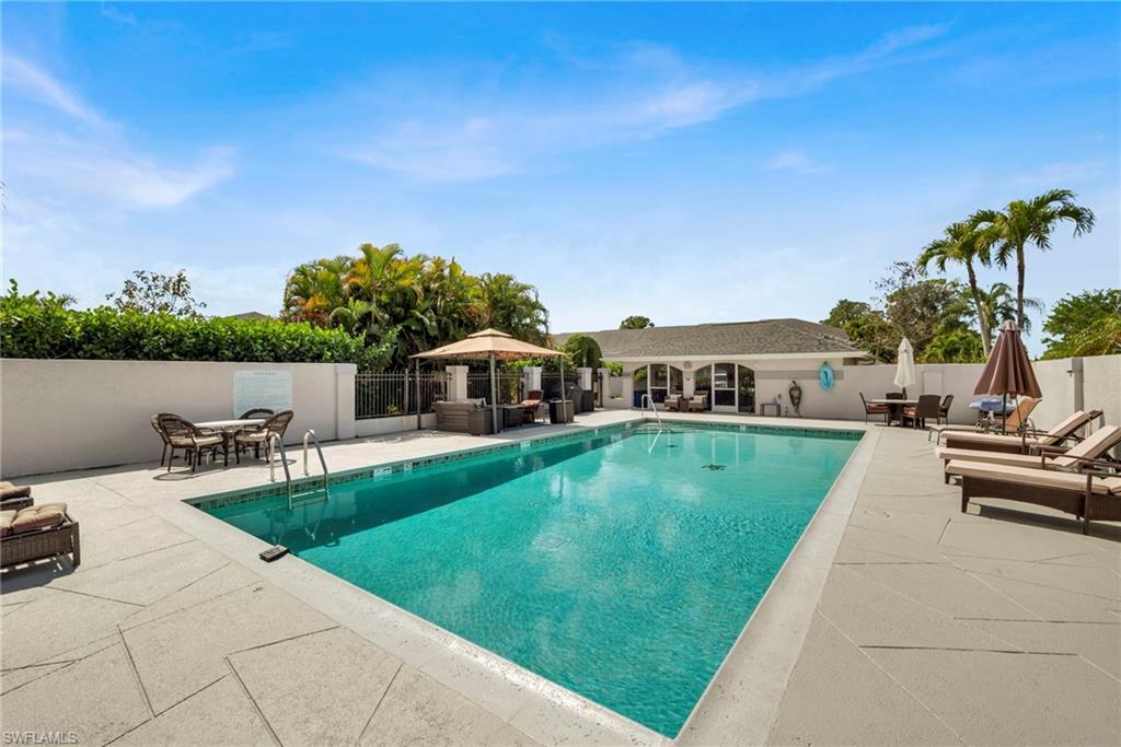 View of community pool with patio surround and outdoor dining area, grill
