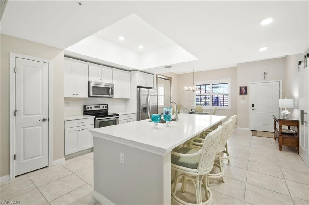 Kitchen featuring a kitchen breakfast bar, stainless steel appliances, light tile patterned floors, and white cabinetry