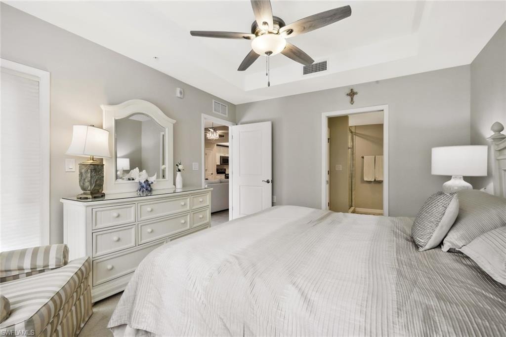 Carpeted bedroom with a ceiling fan, a raised ceiling, and ensuite bath