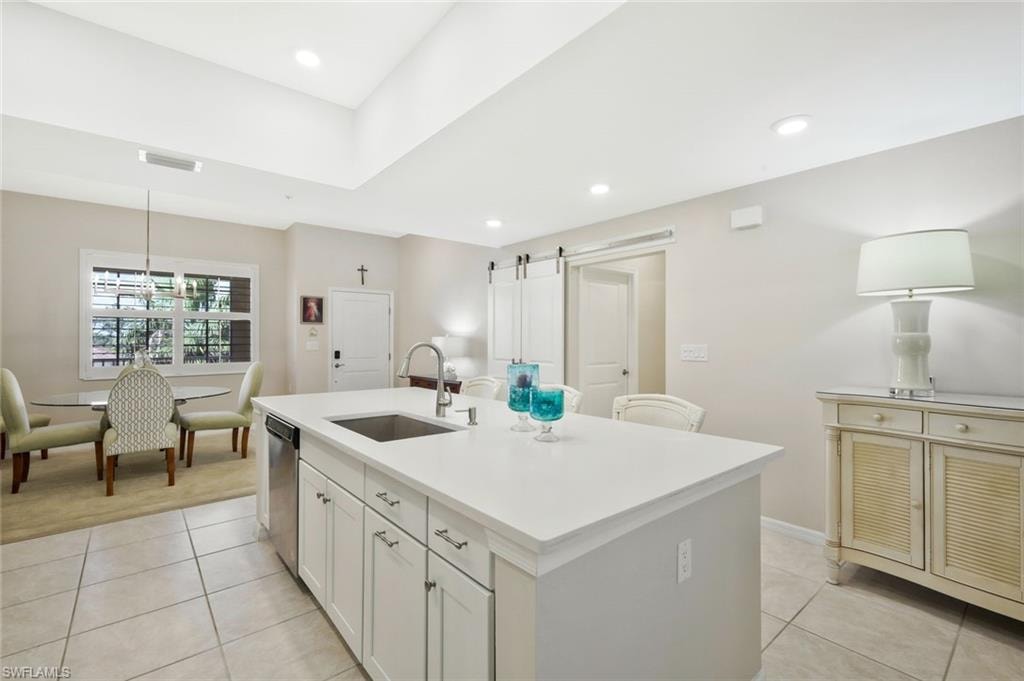 Kitchen featuring a barn door, a center island with sink, light tile patterned flooring, and white cabinetry