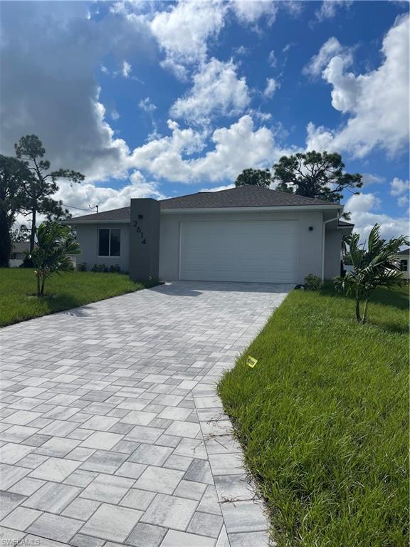 Single story home with a front lawn, an attached garage, stucco siding, and decorative driveway