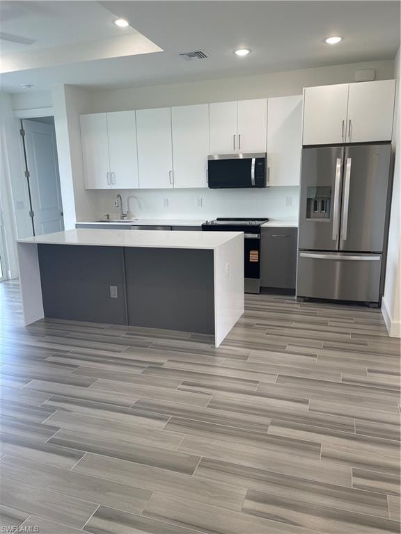 Two tone kitchen featuring fridge, stove, wood tiled floors, recessed lighting, and a center island