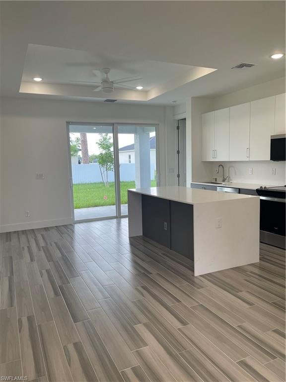 Two tone kitchen with a raised ceiling, stainless steel range, recessed lighting, ceiling fan, and wood finish floors