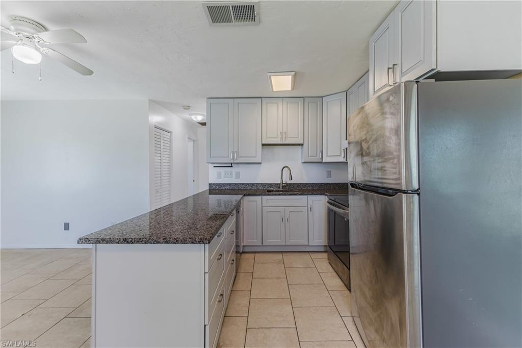 Kitchen with stainless steel appliances, dark stone counters, a peninsula, and light tile patterned floors