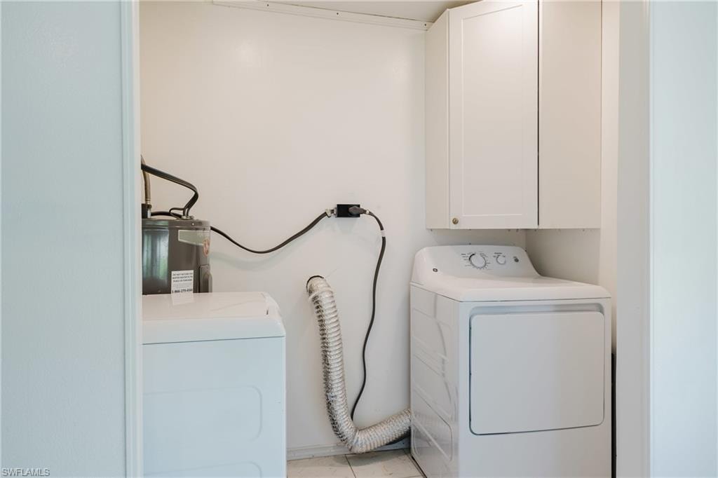 Laundry room with electric water heater, washer and clothes dryer, light tile patterned flooring, and cabinet space