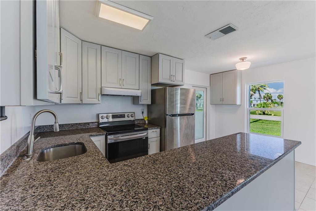 Kitchen with dark stone counters, stainless steel appliances, a peninsula, and white cabinetry