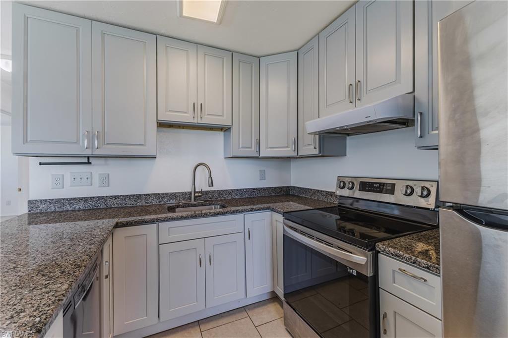 Kitchen with stainless steel appliances, dark stone countertops, and light tile patterned floors