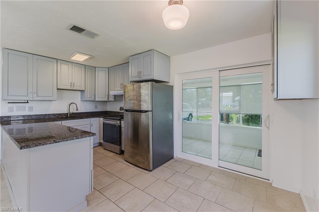 Kitchen with stainless steel appliances, dark stone countertops, a peninsula, and light tile patterned floors
