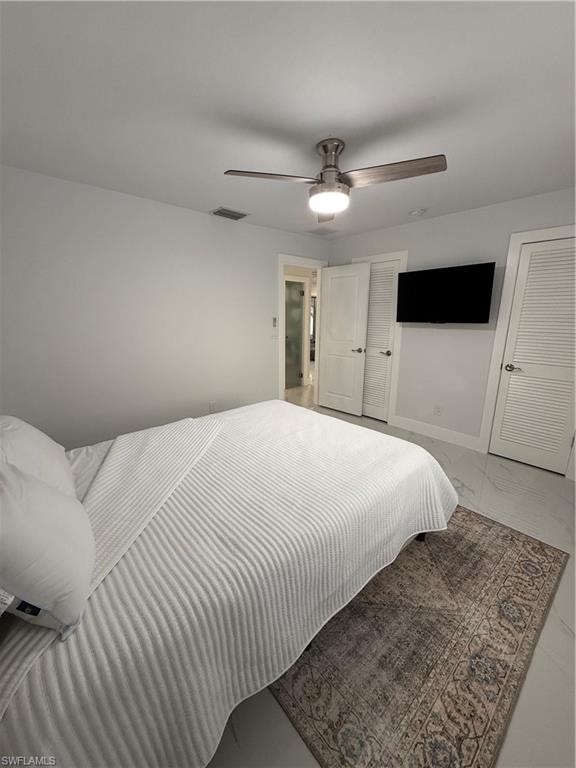 Bedroom with marble finish flooring, ceiling fan, and multiple closets