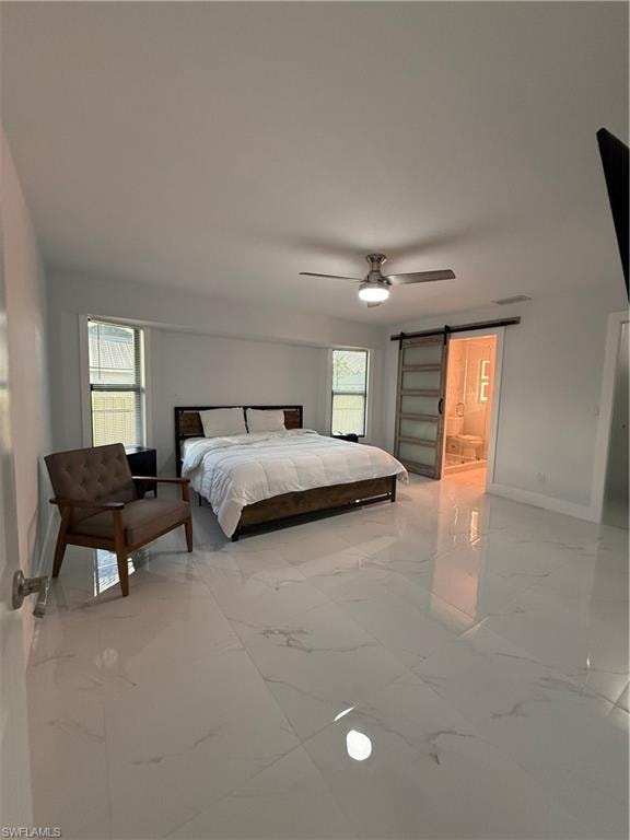 Bedroom featuring a barn door, light marble finish flooring, a ceiling fan, and ensuite bathroom
