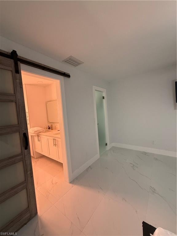 Bathroom with a barn door, light marble finish floors, and ensuite bathroom