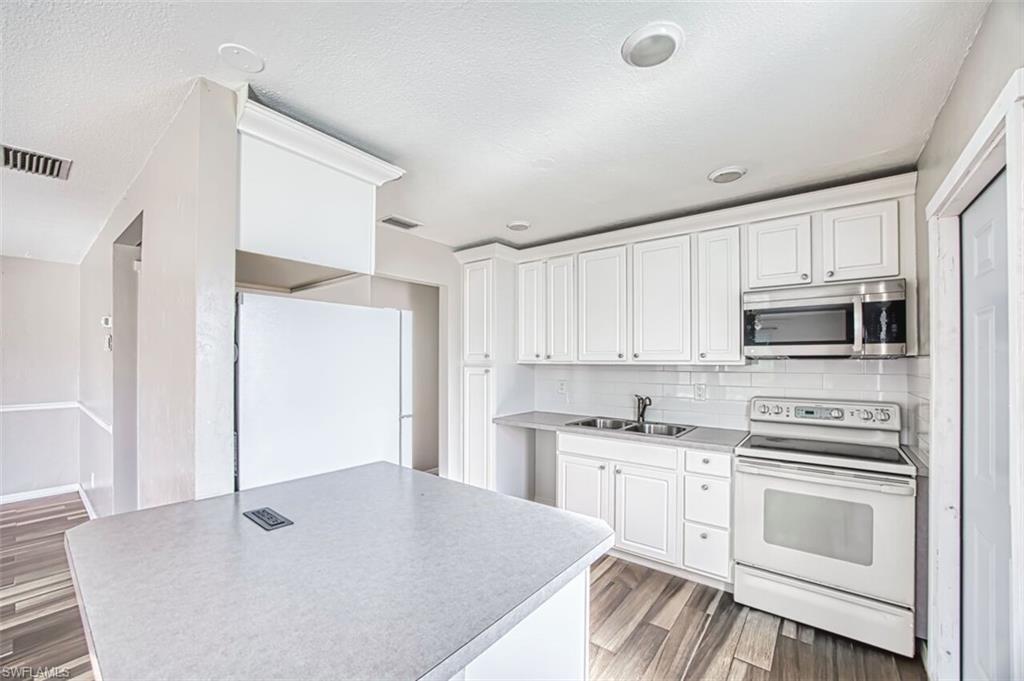 Kitchen featuring white appliances, white cabinets, light wood finished floors, backsplash, and light countertops