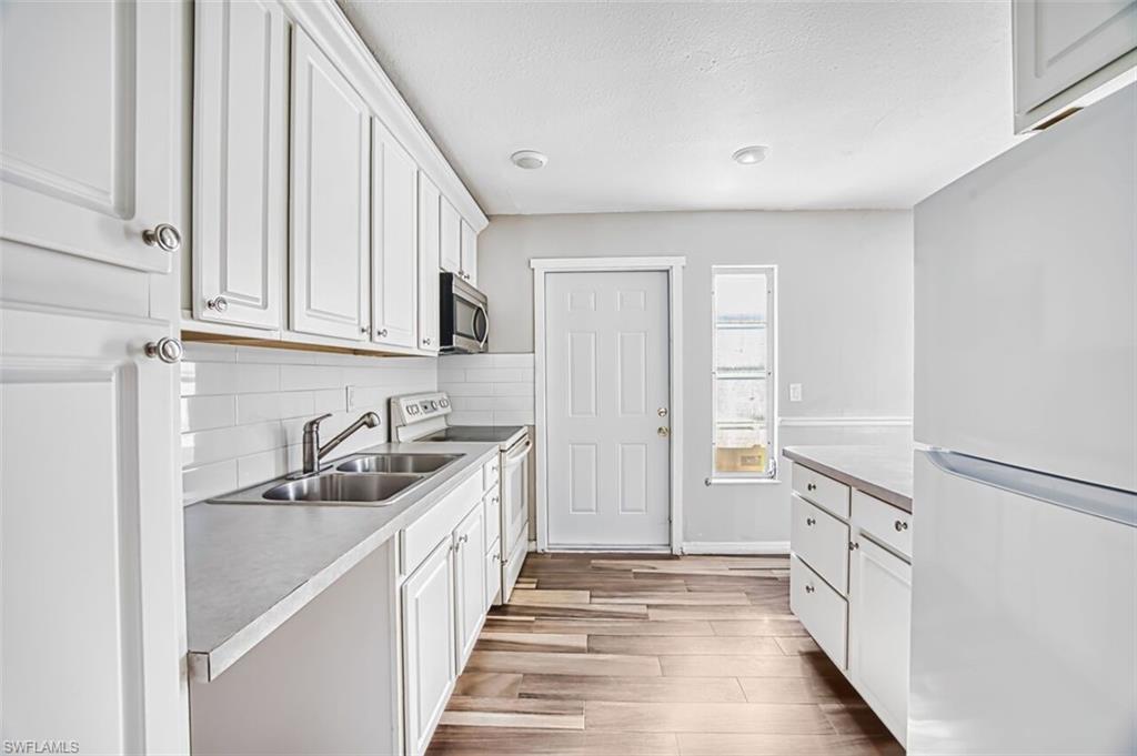 Kitchen featuring white appliances, white cabinetry, light wood-style floors, and light countertops