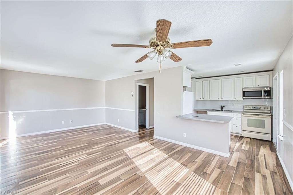 Kitchen with white appliances, white cabinets, ceiling fan, light countertops, and wood finish floors
