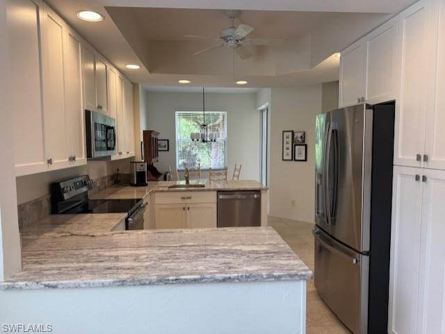 Kitchen featuring stainless steel appliances, a peninsula, light stone countertops, white cabinetry, and ceiling fan