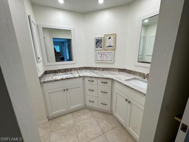 Full bathroom with double vanity, a textured wall, light tile patterned flooring, and recessed lighting