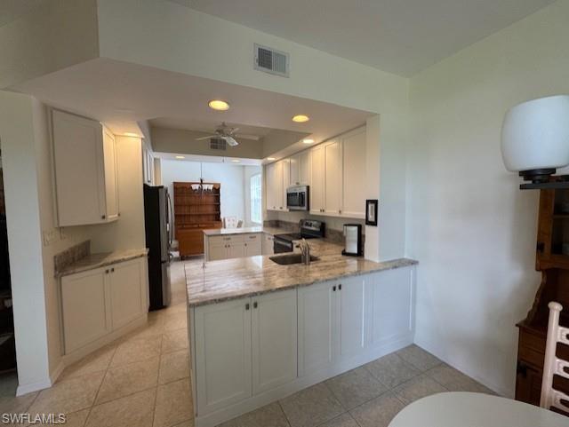 Kitchen featuring a peninsula, light stone countertops, stainless steel appliances, white cabinets, and ceiling fan