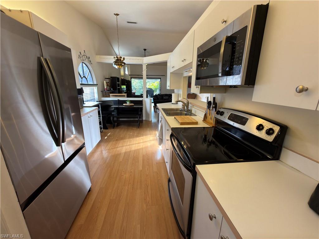 Kitchen featuring stainless steel appliances, lofted ceiling, light countertops, white cabinetry, and light wood-type flooring
