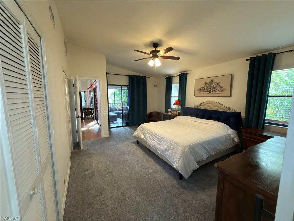 Bedroom with a barn door, vaulted ceiling, carpet floors, a ceiling fan, and ensuite bath