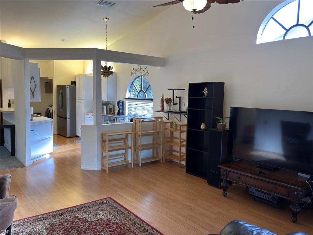 Living room with hanging lights, light wood-style flooring, a ceiling fan, and vaulted ceiling