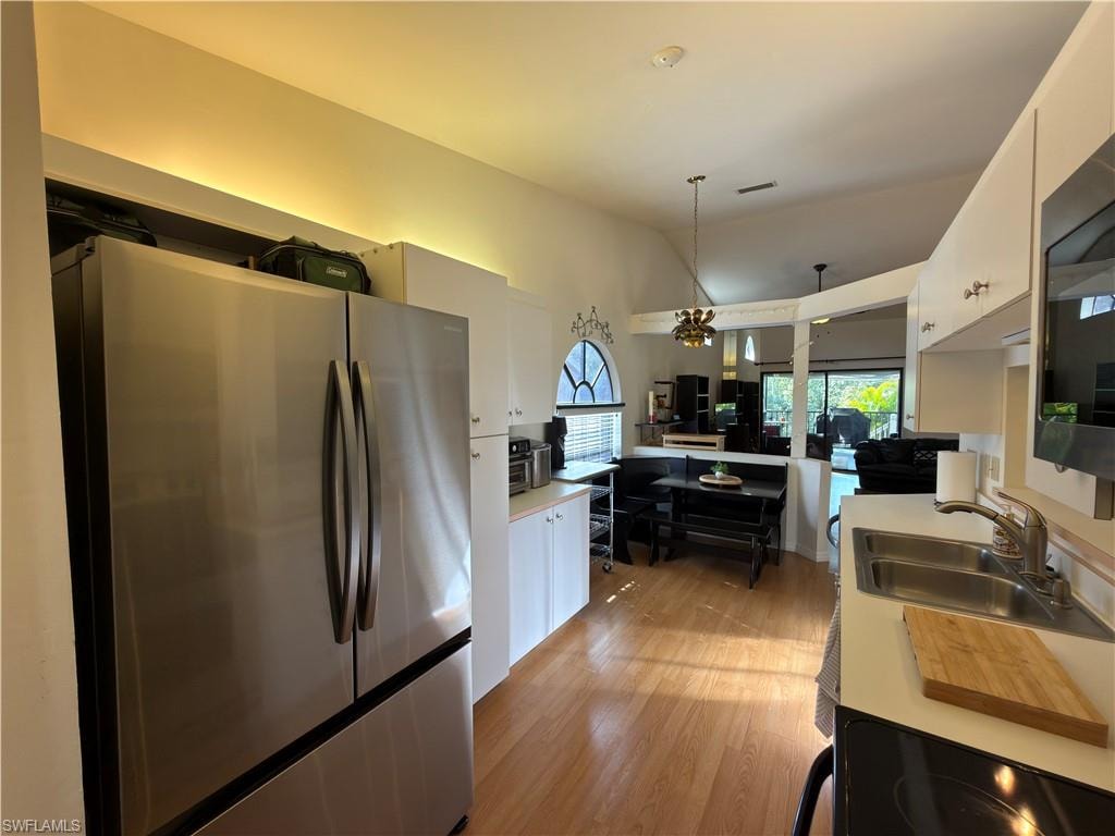 Kitchen with black appliances, a chandelier, light countertops, light wood finished floors, and white cabinets