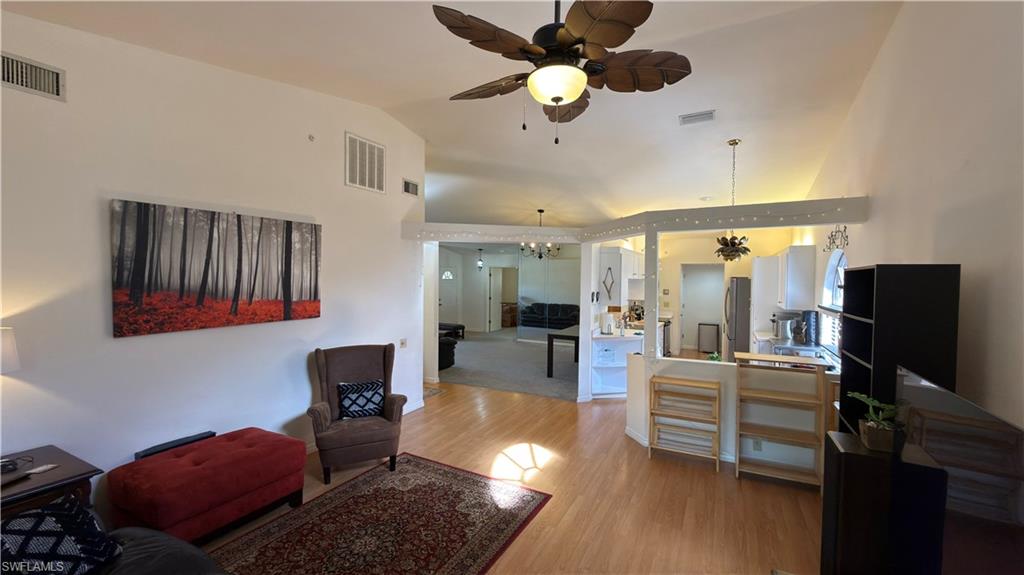 Living room with a ceiling fan, light wood-style floors, hanging lights, and vaulted ceiling
