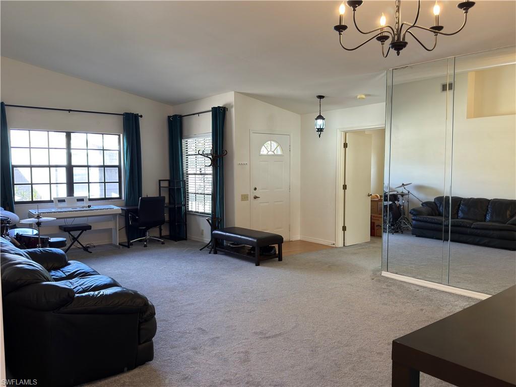 Living room with lofted ceiling, light colored carpet, hanging lights, and a desk