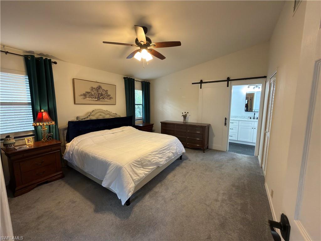 Bedroom with a barn door, vaulted ceiling, carpet floors, a ceiling fan, and ensuite bath