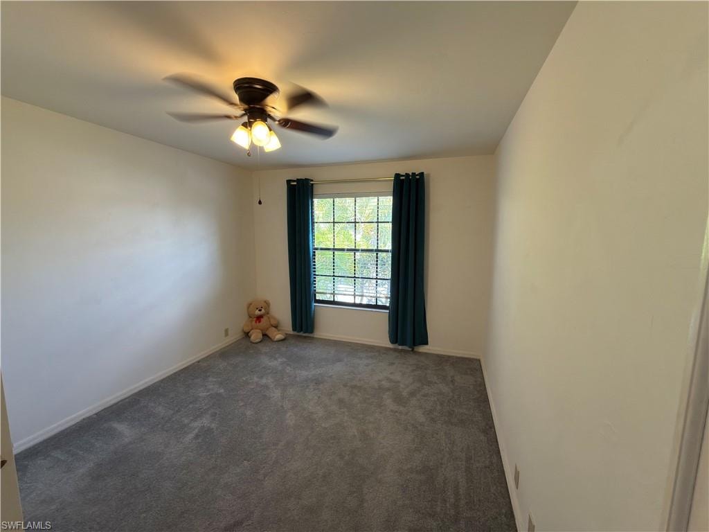 Empty room with dark carpet and a ceiling fan