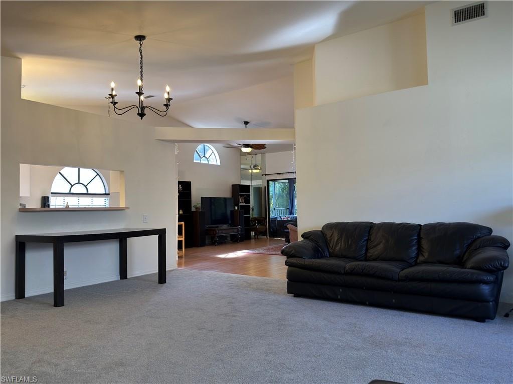 Carpeted living area with a chandelier, a ceiling fan, and vaulted ceiling