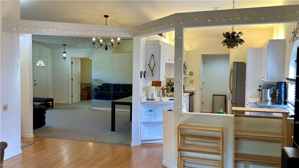 Kitchen with hanging lights, white cabinets, light countertops, stainless steel appliances, and light wood finished floors