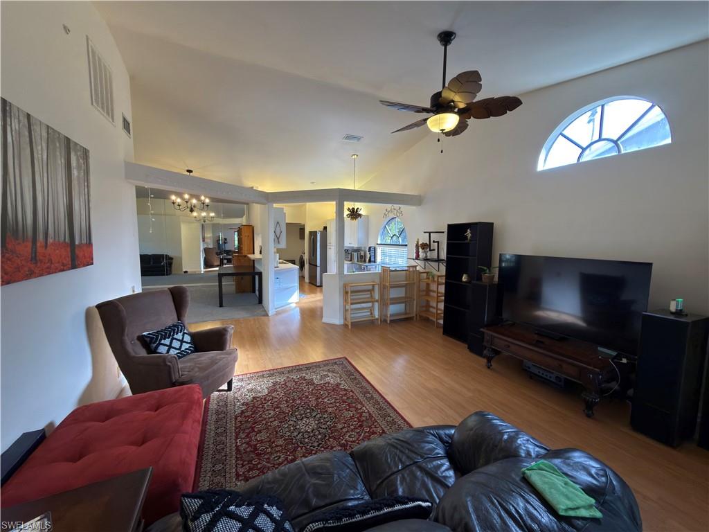 Living area featuring light wood finished floors, hanging lights, ceiling fan, and vaulted ceiling
