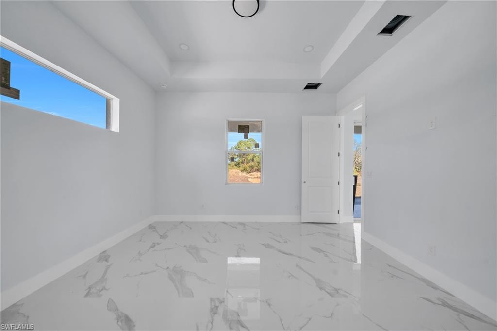 Unfurnished bedroom with a tray ceiling and light marble finish flooring